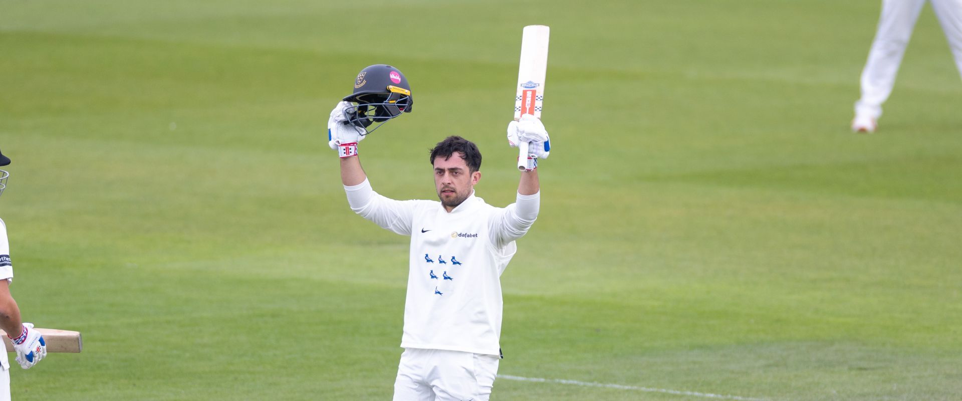 Tom Haines raises his helmet and bat to celebrate reaching his century against Somerset.