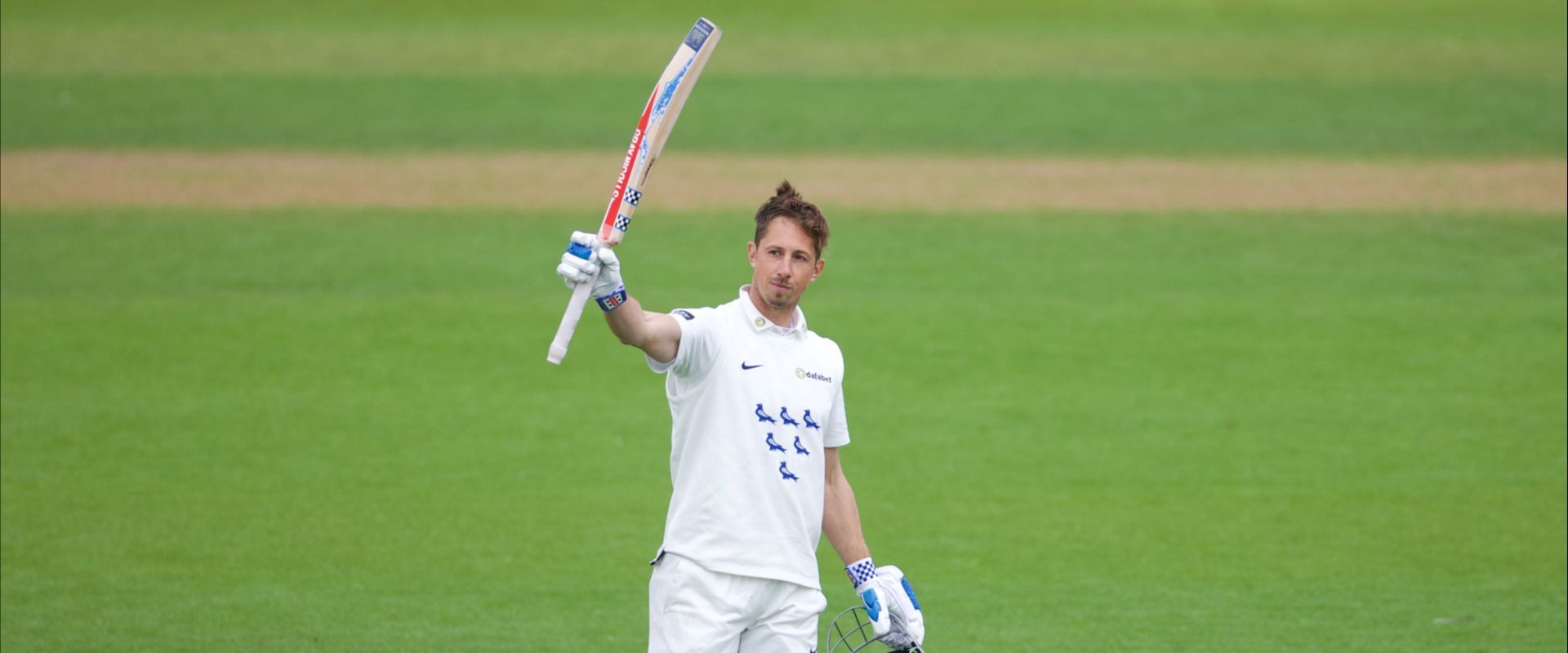 John Simpson raises his bat after reaching his century.