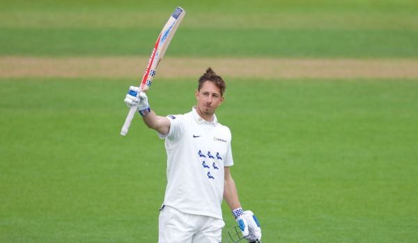 John Simpson raises his bat after reaching his century.